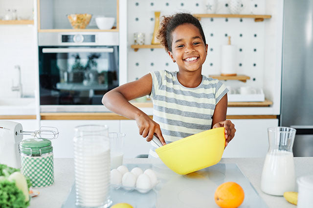 a young girl using a mixing bowl in a kitchen