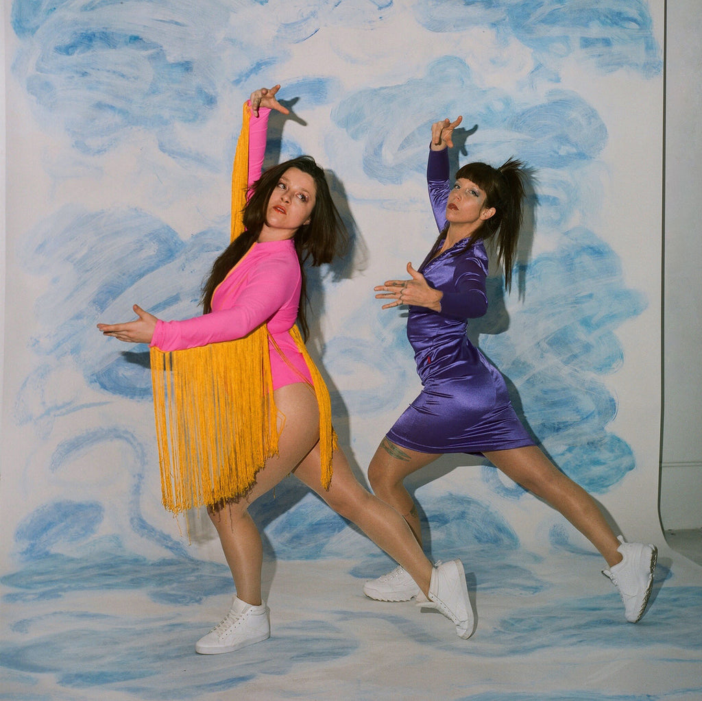 models in synchronized arm up dancers pose ice skating inspired suits in front of cloud painted set.