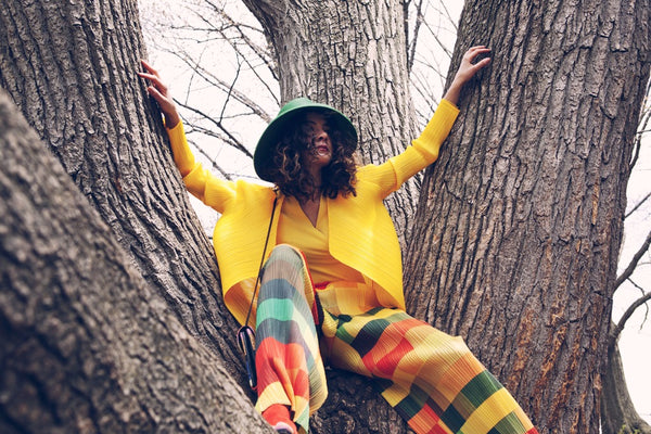 model sits in tree in pleats please and conceptual hat.