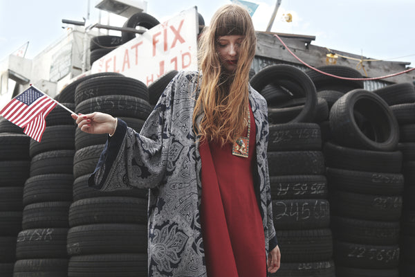 zuzu wearing red dress and blue robe in front of tires 