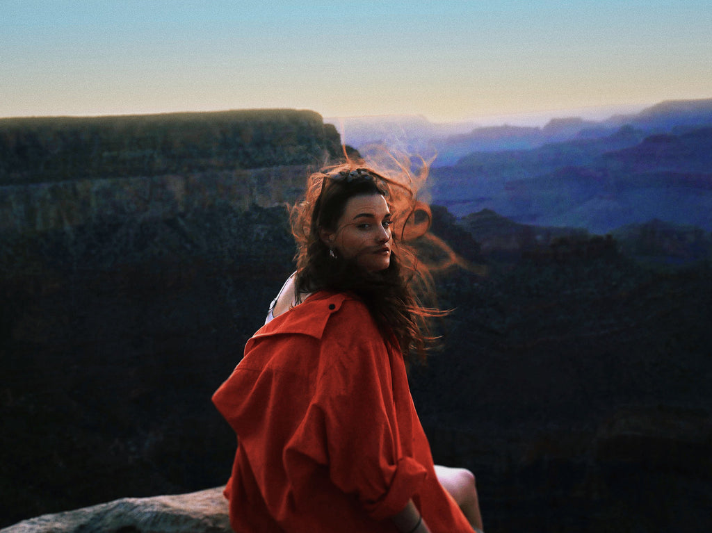 a person sitting on a cliff overlooking the grand canyon.