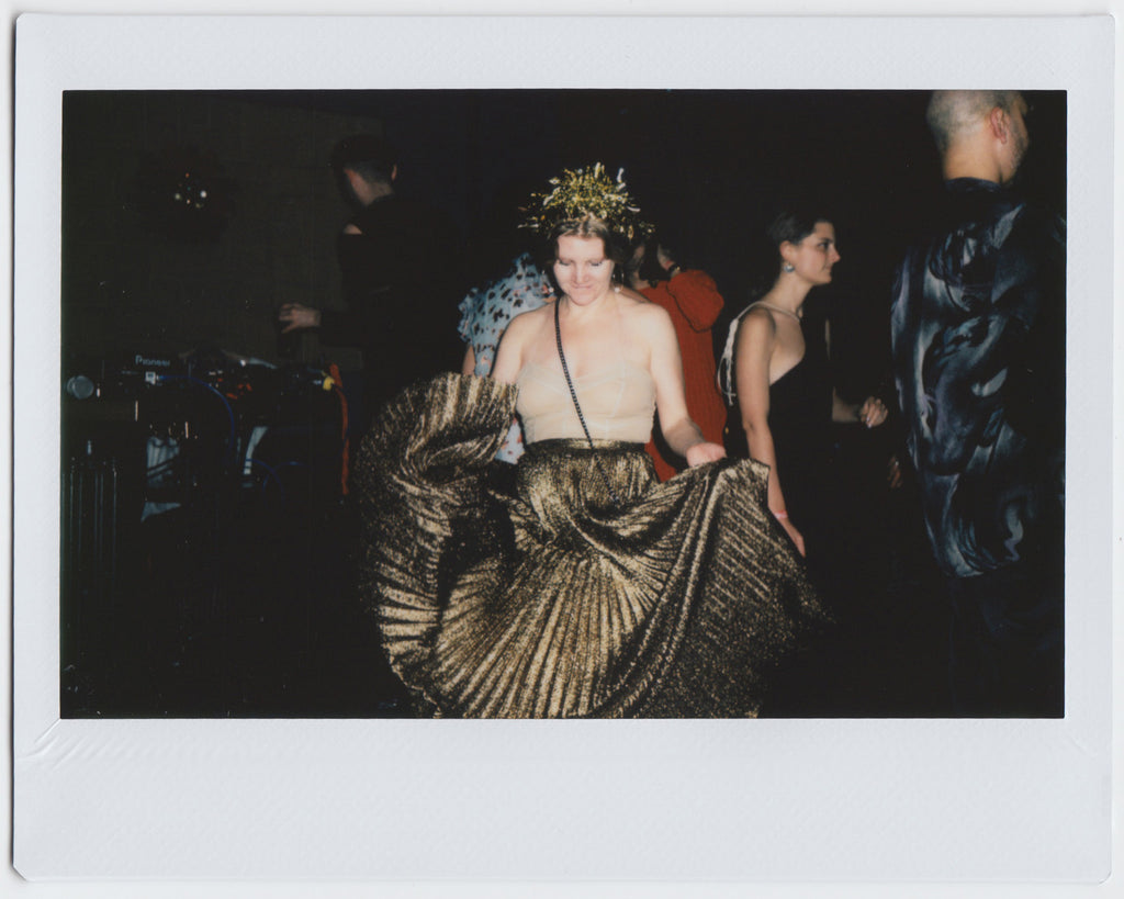 person wearing gold outfit on dance floor, moving maxi skirt, looking down - polaroid style. 