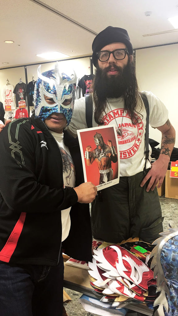 two people posing for a photo in front of a table full of wrestling memorabilia.