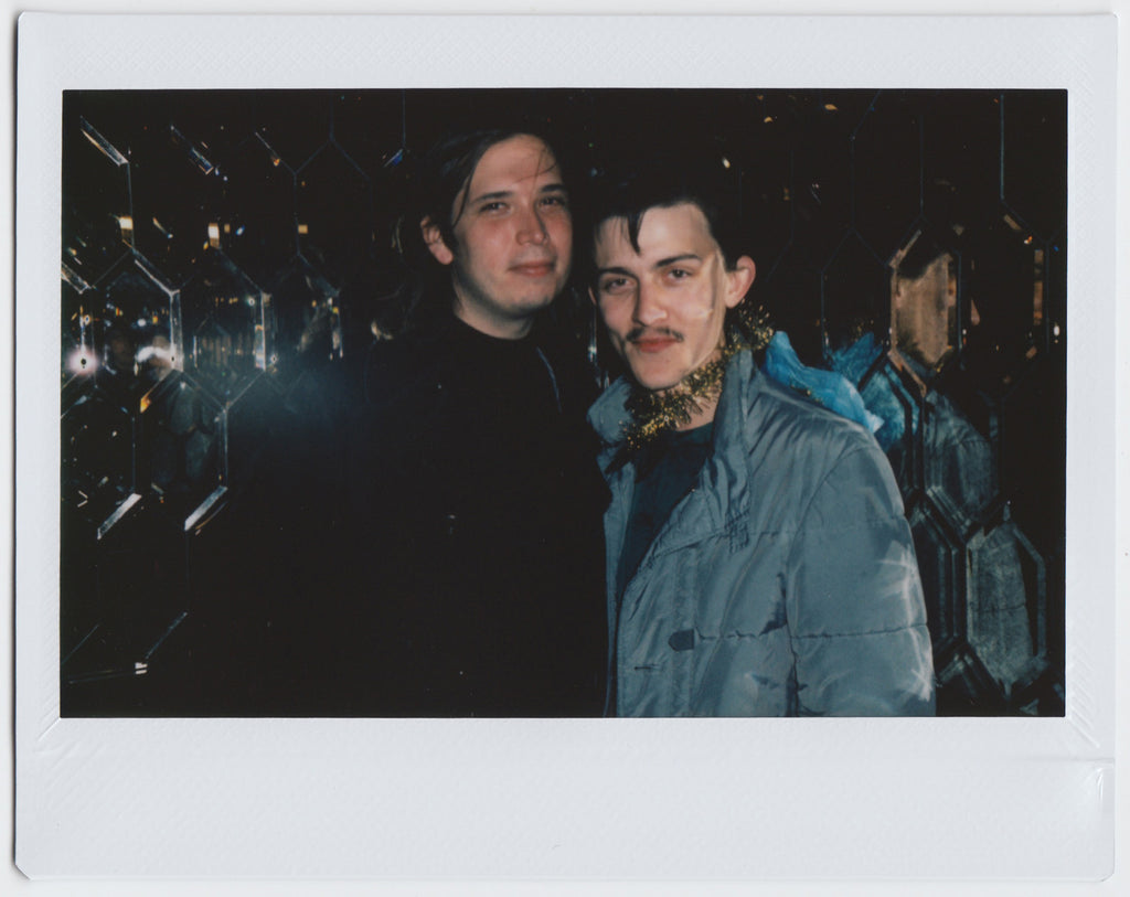 duo posing with slight smiles, mirrored wall in background - polaroid style. 