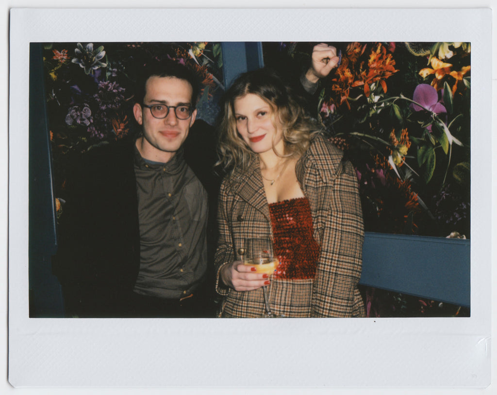 duo posing, slightly smiling, one holding drink - polaroid style. 