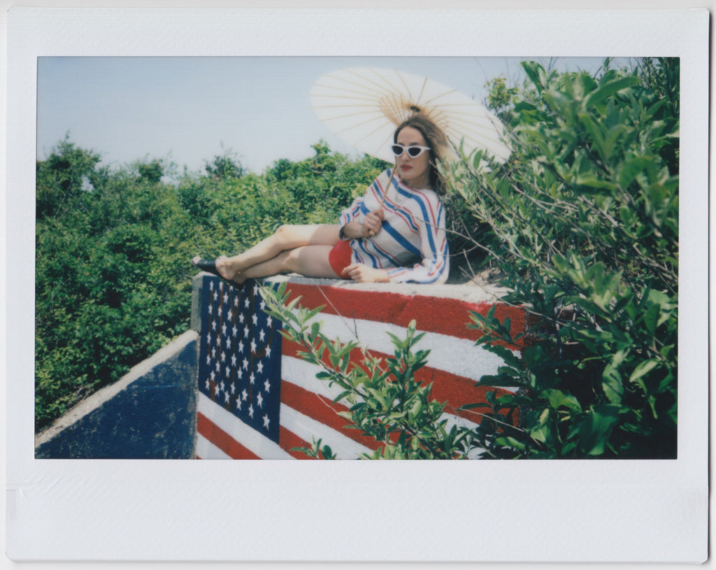 model with paper umbrella in red white and blue lying on top of an american flag. 