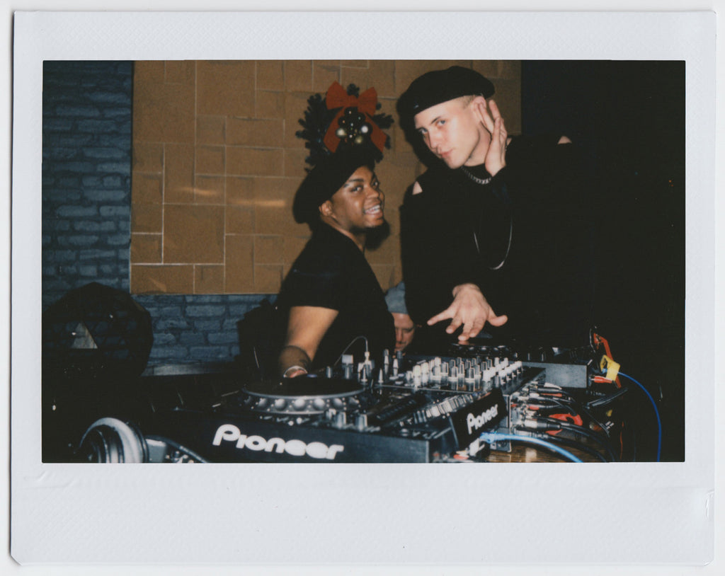 duo posing by dj equipment, pretending to play, with a christmas ornament in the background - polaroid style. 