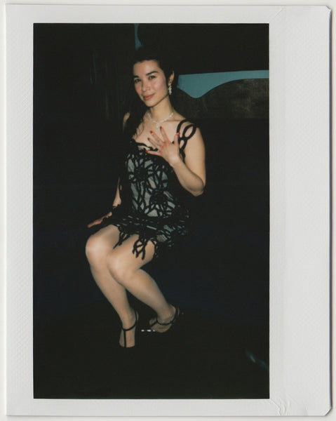 employee seated, posing with left hand on left bust, full body shot – polaroid style.