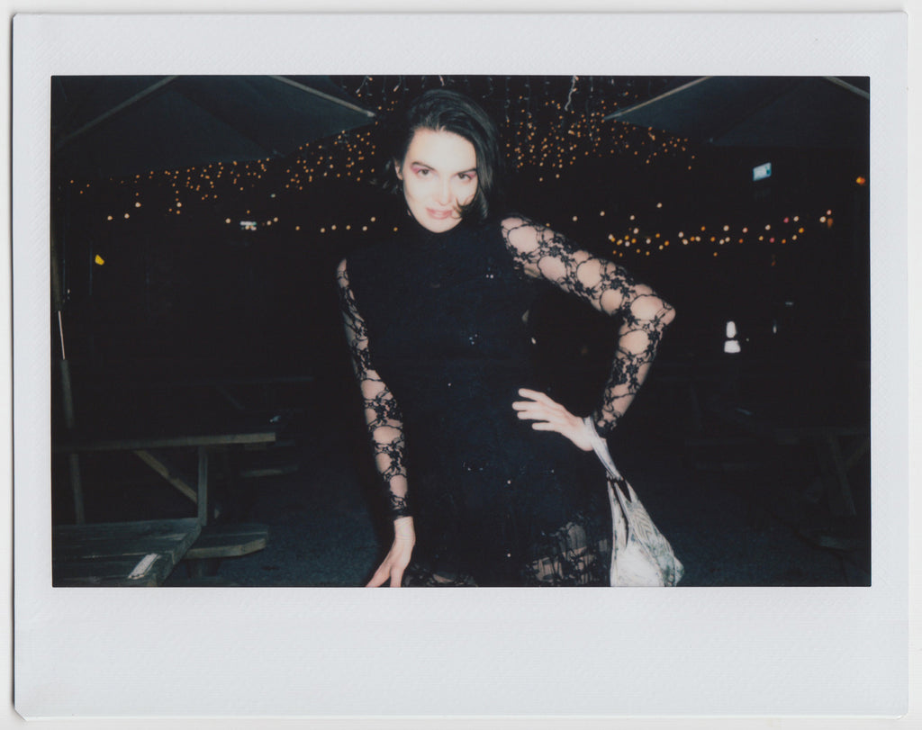 person posing, with left hand at waist, lights at background - polaroid style. 