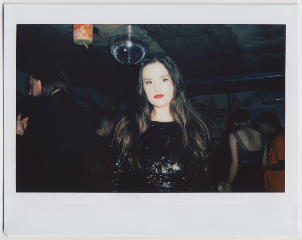 person looking at camera, with disco ball in the background - polaroid style. 