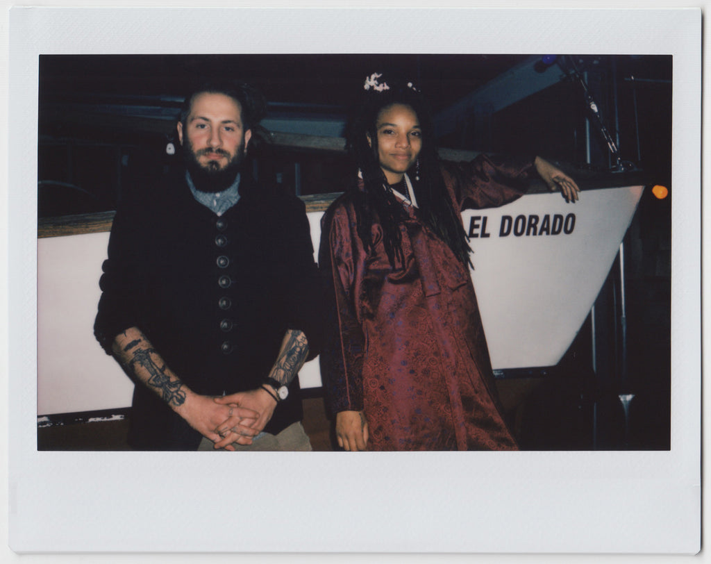 duo posing leaning against a boat, looking directly at camera - polaroid style. 