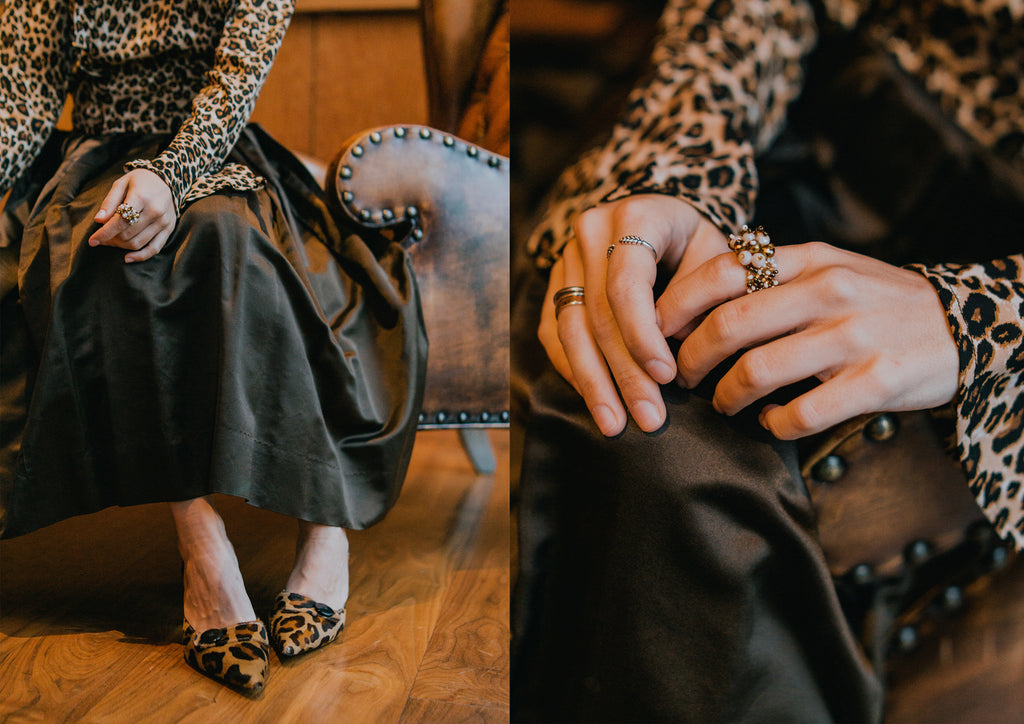 details of leopard print top, brown skirt and leopard print heels sitting at a bar.