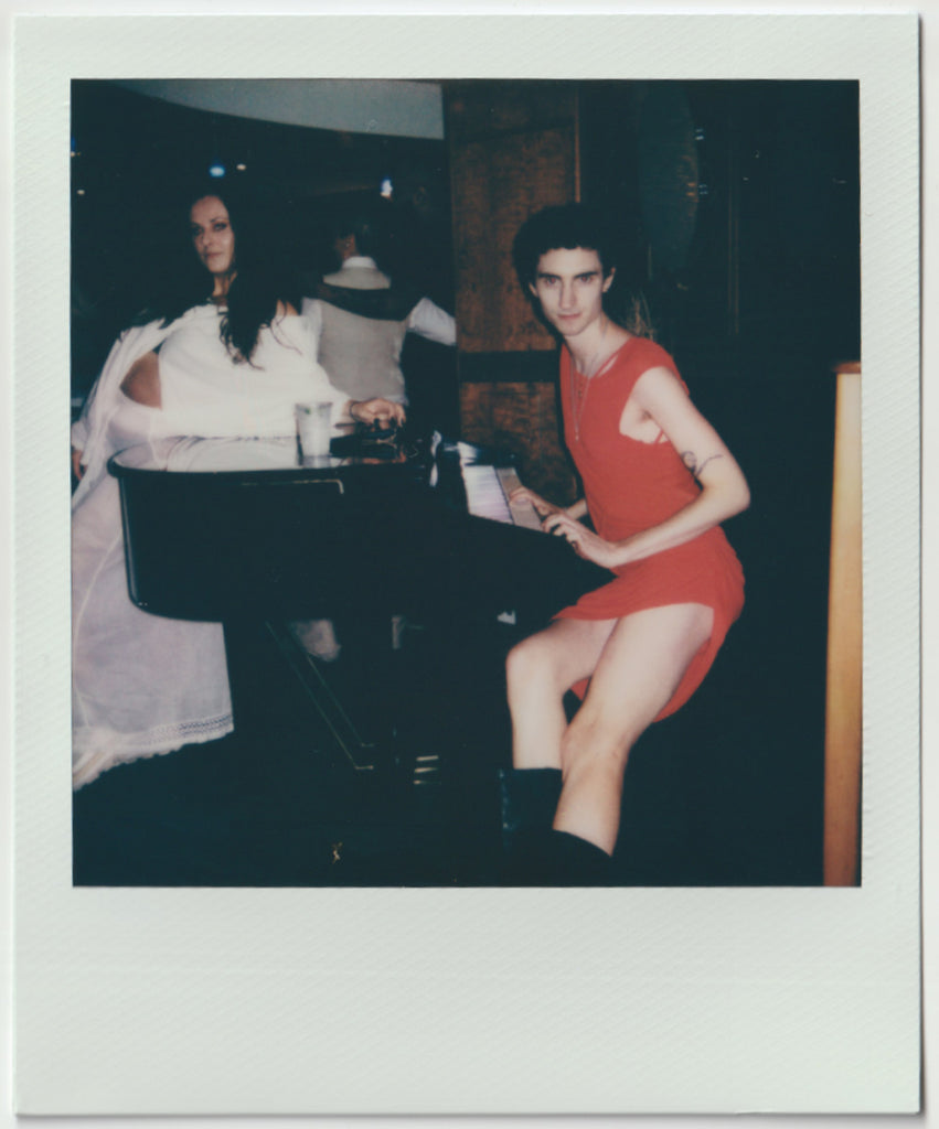 employee playing piano and posing to the camera in a red dress.