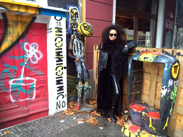 person posing in all black outfit next to street art. 