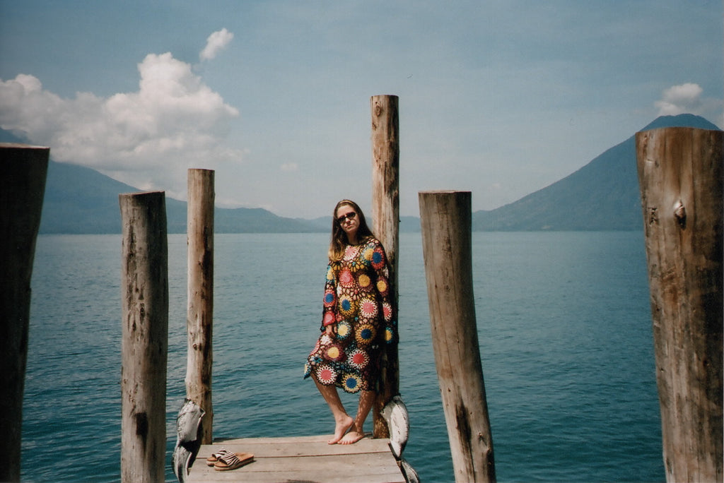person with crochet dress standing on a dock next to a lake.