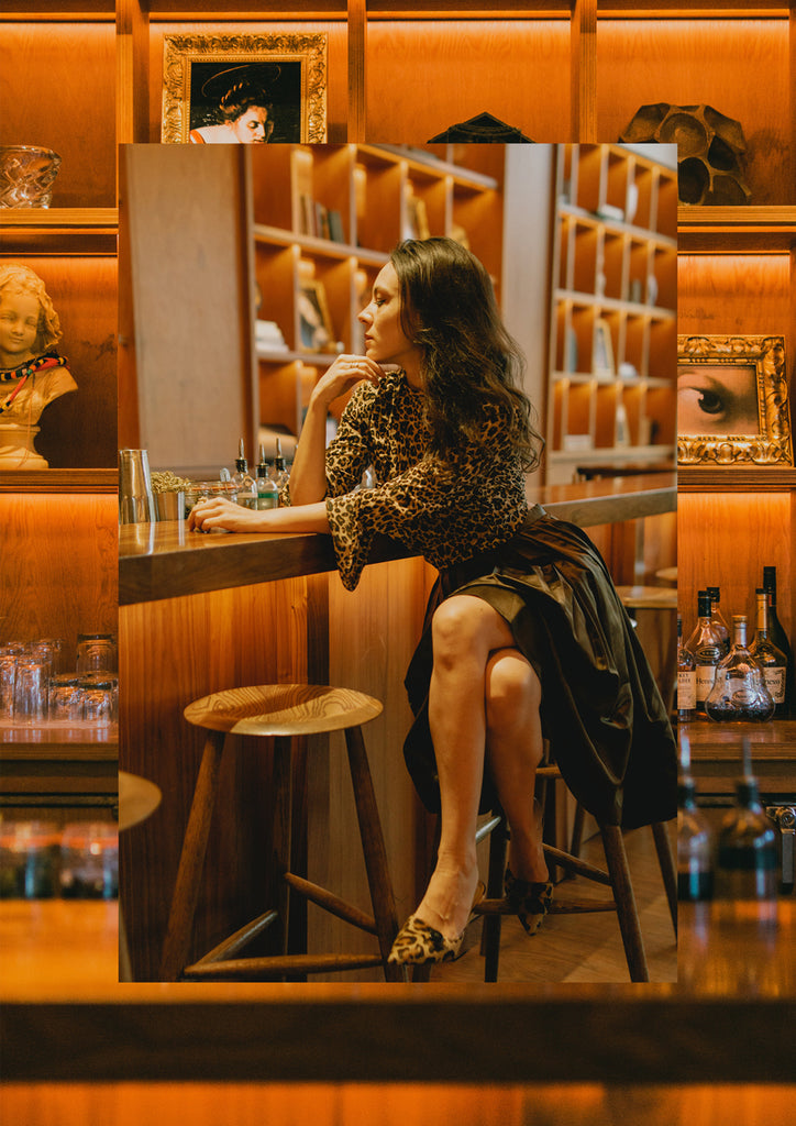 sarah amorelli in leopard print top, brown skirt and leopard print heels sitting at a bar.