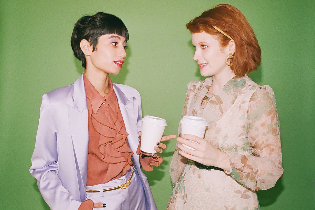 two models chatting to each other with coffee cups. 