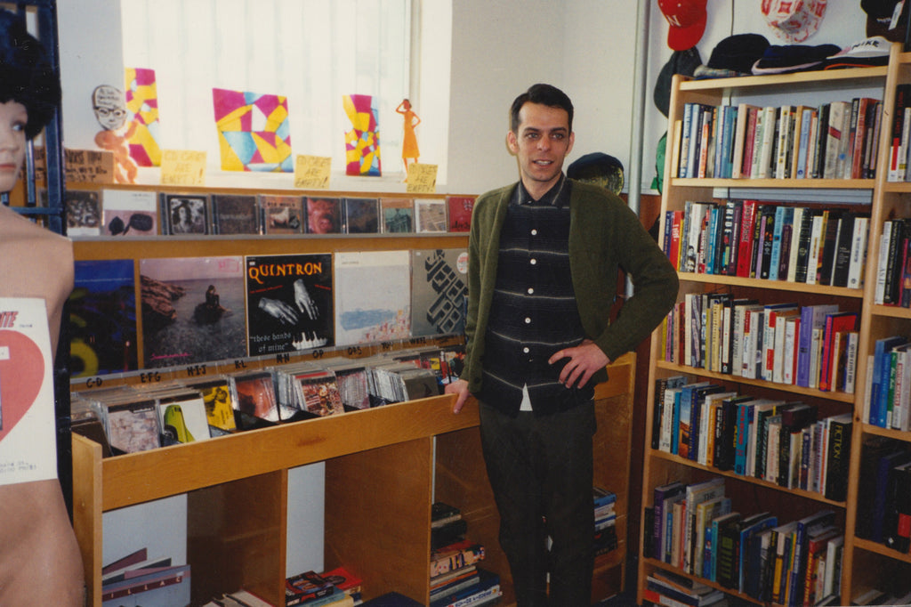 sam wearing a cardigan standing in front of his curated record section