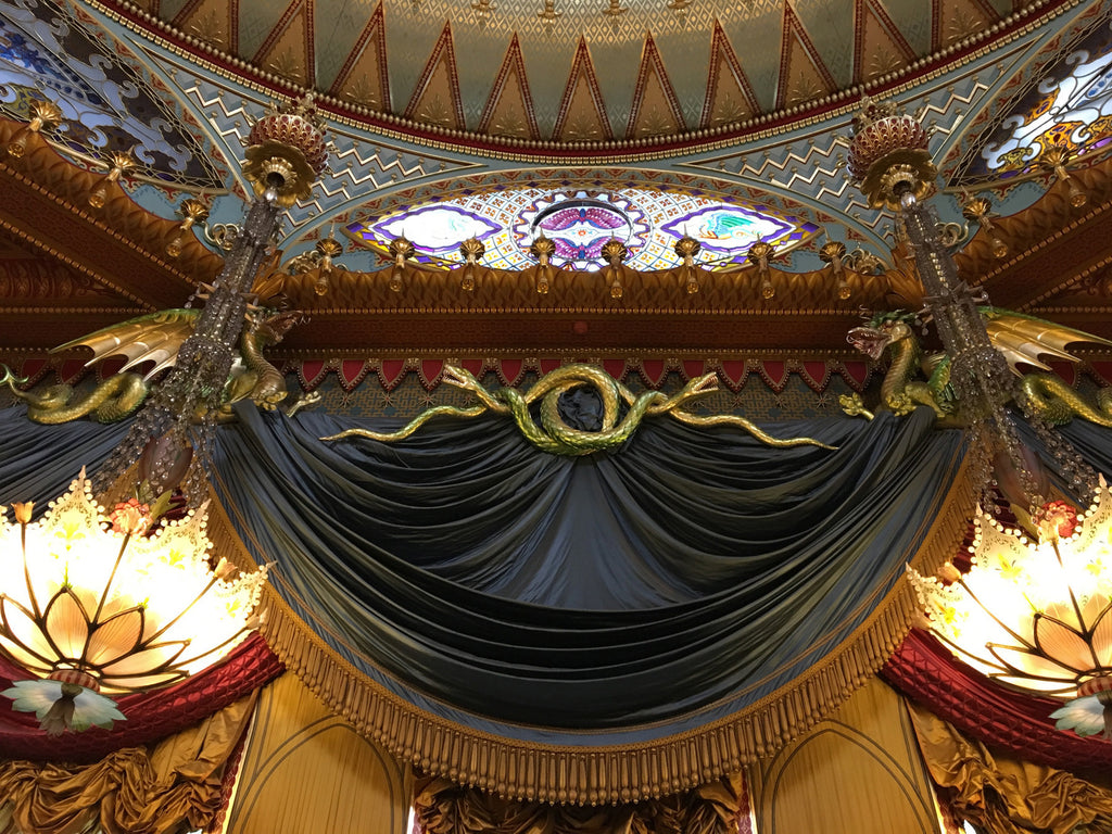 the ceiling of an ornate building with a chandelier and drapes.