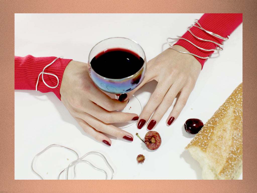 still life of hands in bracelets with glass of wine and cherries.