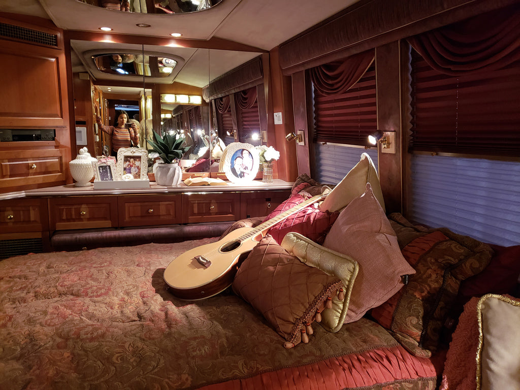 person reflection in mirror at tour bus, and guitar on bed.