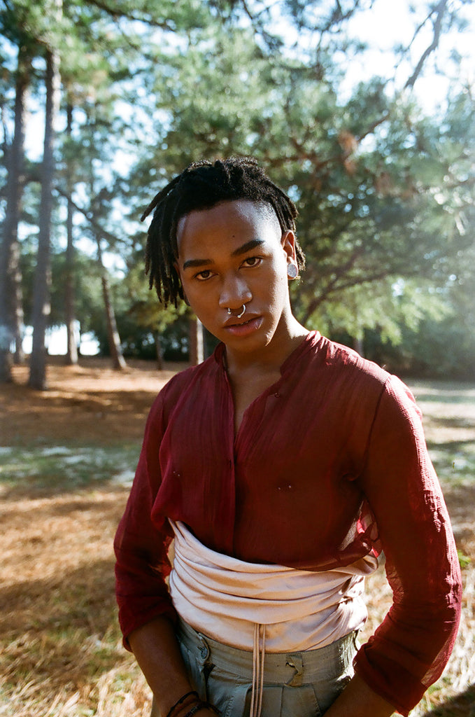 a person in a red shirt standing in a wooded area.