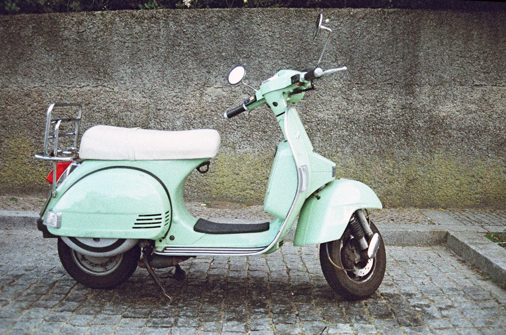 a green scooter parked on a cobblestone street.