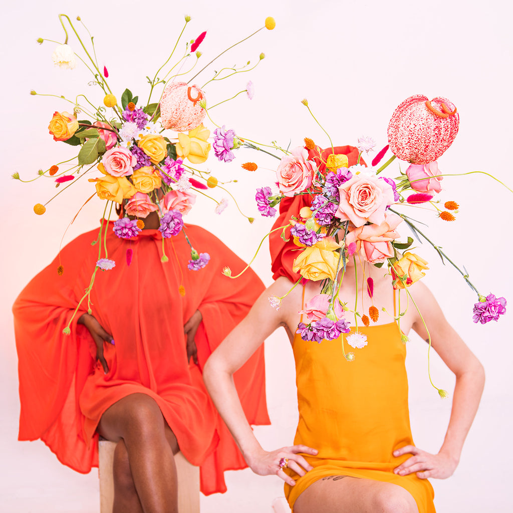 two models seated with flower bouquets covering their face.