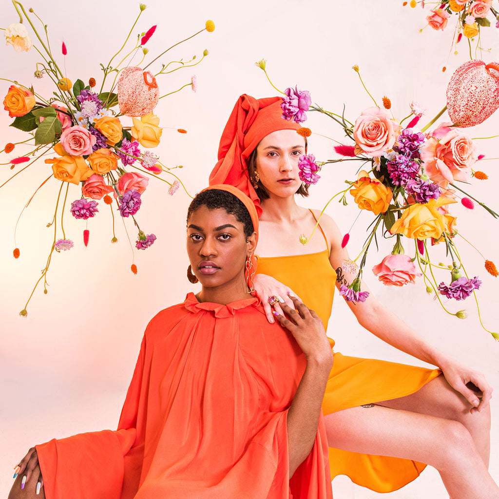 two models seated posing amongst floral arrangements. 