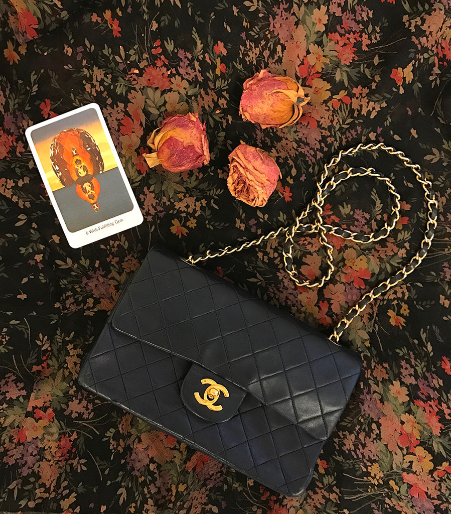 still life of a wish fulfilling gem card, chanel bag and dried roses.