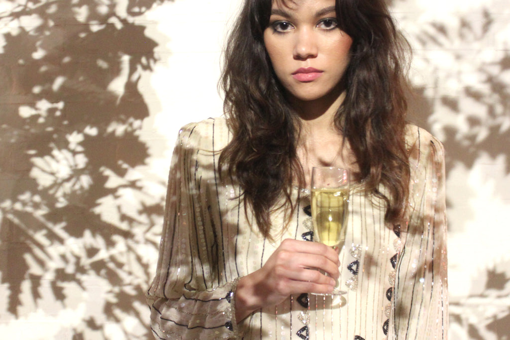 model with champagne against wall with shadows from a tree.