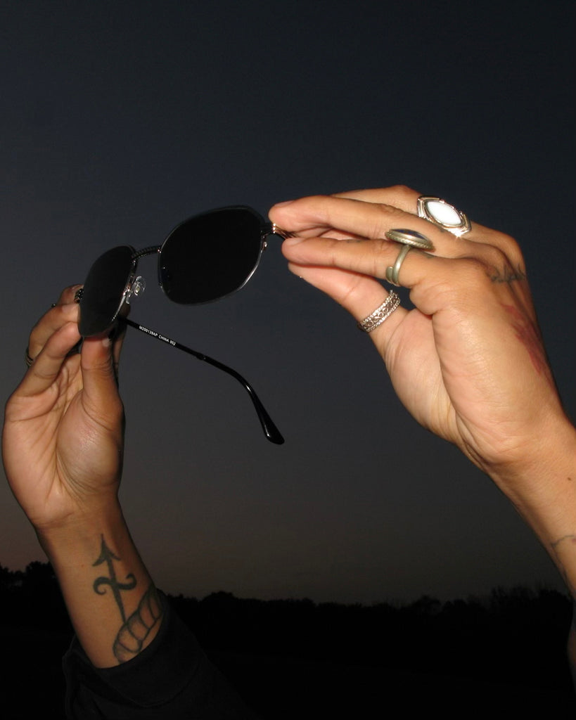 detail of hands holding up sunglasses and featuring rings. 