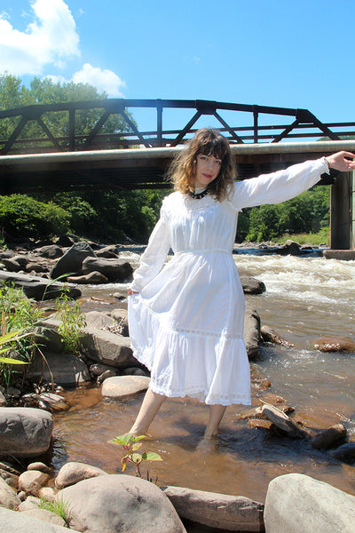 person in a white dress posing at river, bridge in the background.