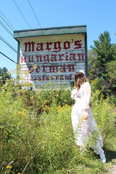 person posing in front of 'margo's hungarian german' sign.
