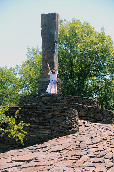 a person in a white dress is standing on top of a stone cross.