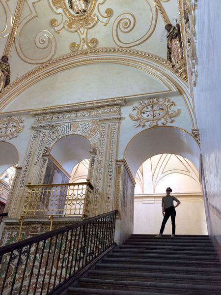 person with hand on waist posing on stairs inside santo domingo, featuring gold details.