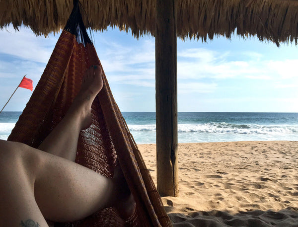 legs resting in a hammock with a beach view ahead.
