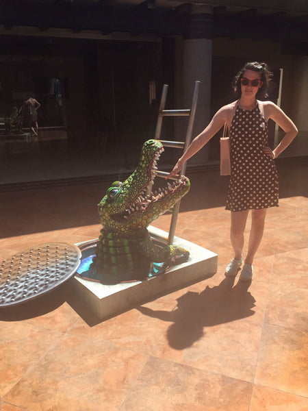 full-body shot of person pointing a finger into the mouth of a crocodile sculpture.