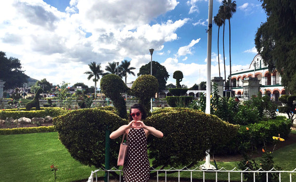 person making heart gestures to the camera, with swan-shaped plant sculptures in the background.