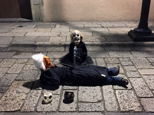children in scary costumes, one lying on the street while the other pretends to wield a sickle over them.