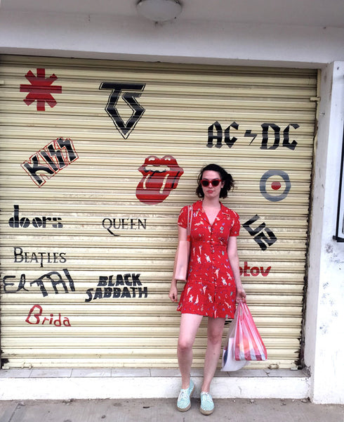 full-body shot of person in all-red outfit holding shopping bags, with a door featuring band symbols like ac/dc, queen, and the doors in the background.