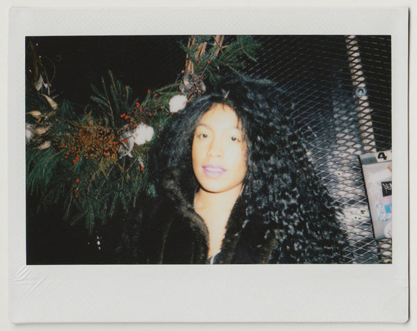 person posing for the camera, smiling with flowers in the back- polaroid style. 