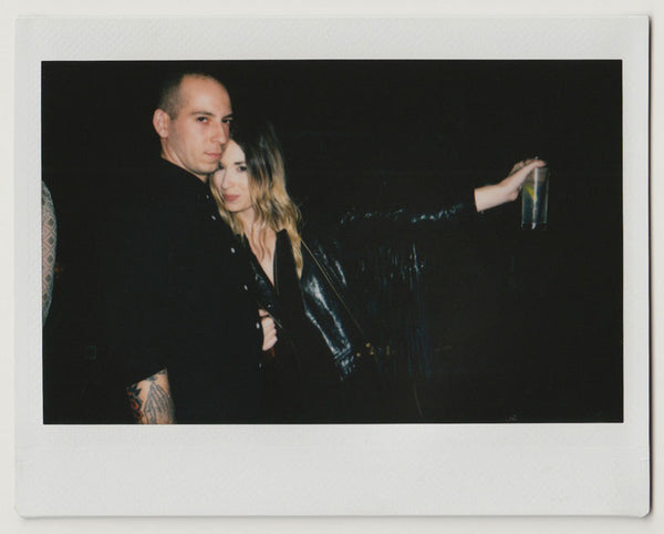 two people posing closely, one with left arm up holding drink – polaroid style.