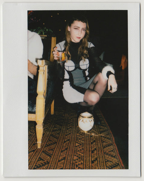 person posing with drink in hand, bag on top of rug – polaroid style.