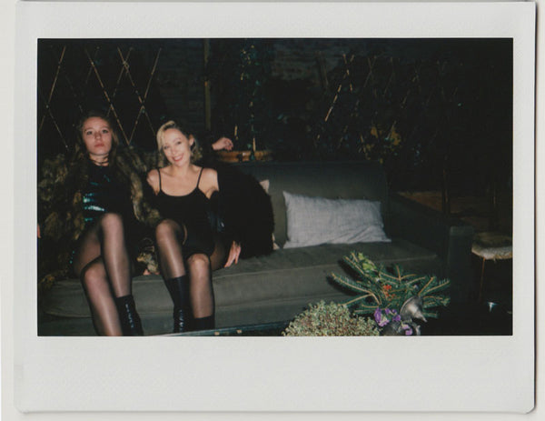 two employees posing, seated on a sofa with flowers on table -polaroid style.