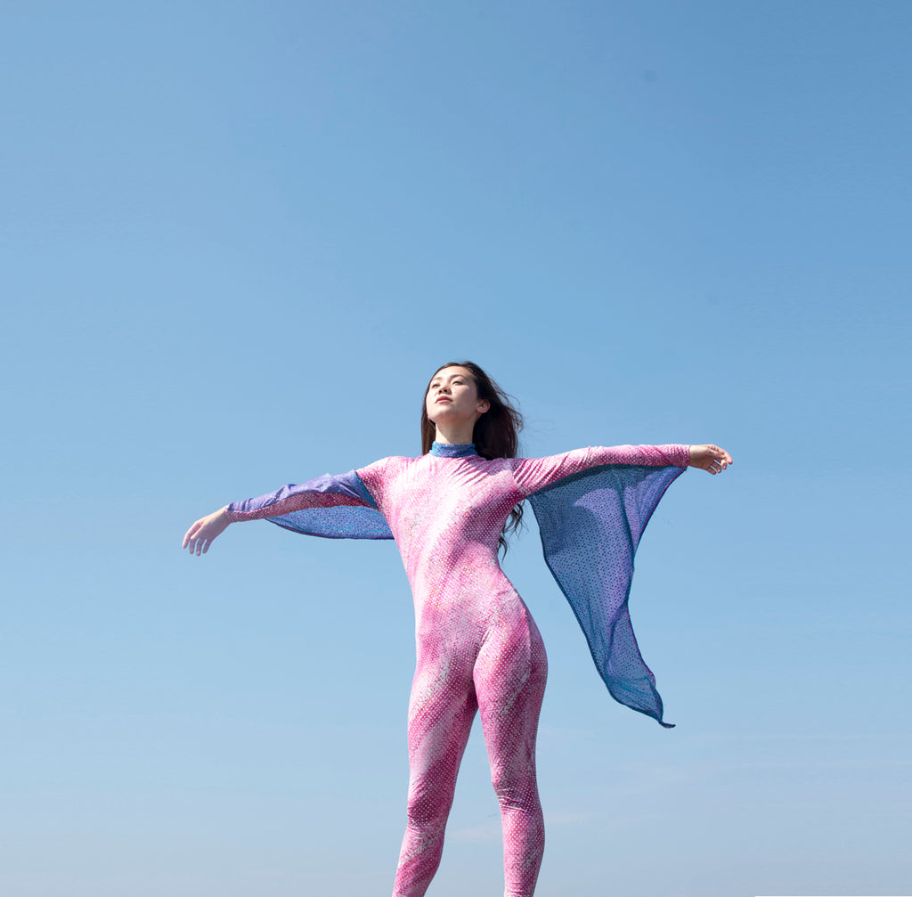 a person in a pink suit standing on top of a rock, blue sky.