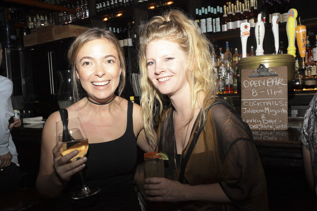 duo smiling, holding drinks with drink menu in the background.