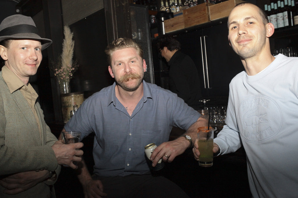 trio posing, holding their drinks - bar in the background.