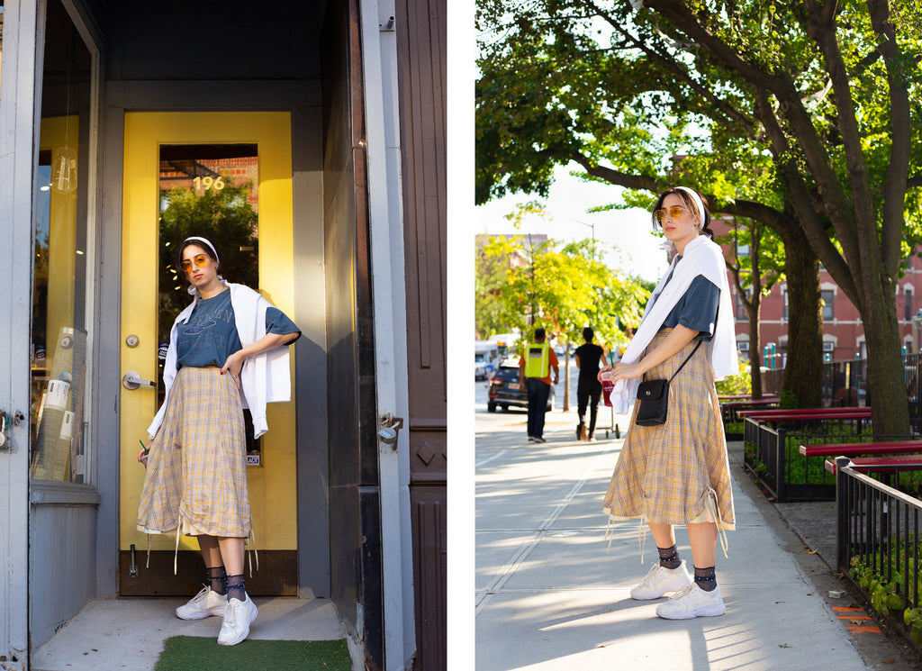 toiby in plaid skirt and t-shirt standing in front of building door and toiby on city sidewalk with sweatshirt worn on shoulders..