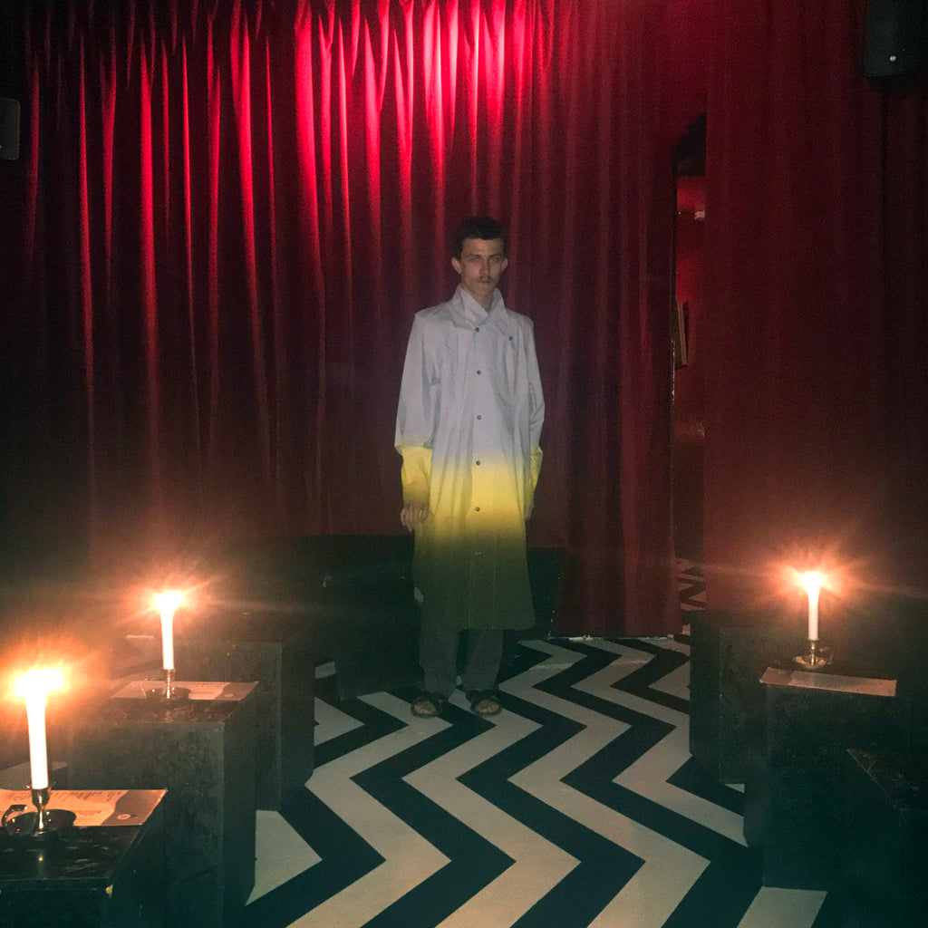 a person in a yellow gradient coat standing in a room with candles.
